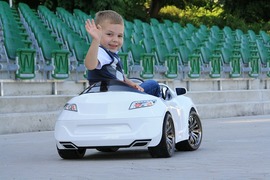 おもちゃの車に乗って後ろを向いて手を降っている子供の写真